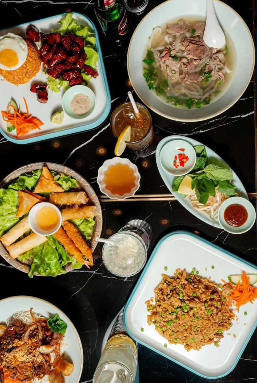Table set with spring rolls, phở and sides